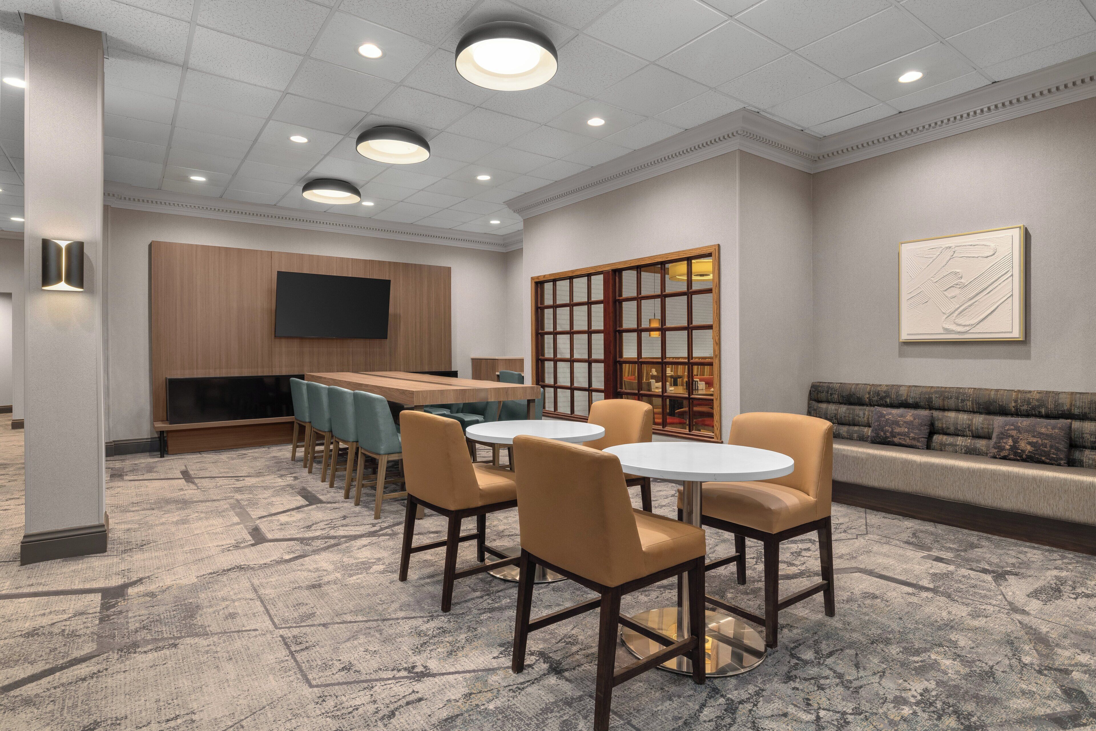 A modern conference room with a round table, chairs, a sofa, and a television on the wall.
