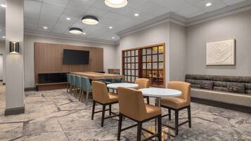 A modern conference room with a round table, chairs, a sofa, and a television on the wall.