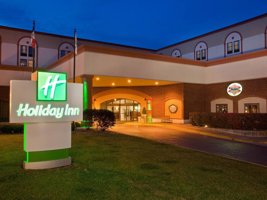 A Holiday Inn hotel entrance with a prominent sign, brick facade, and a well-lit driveway.