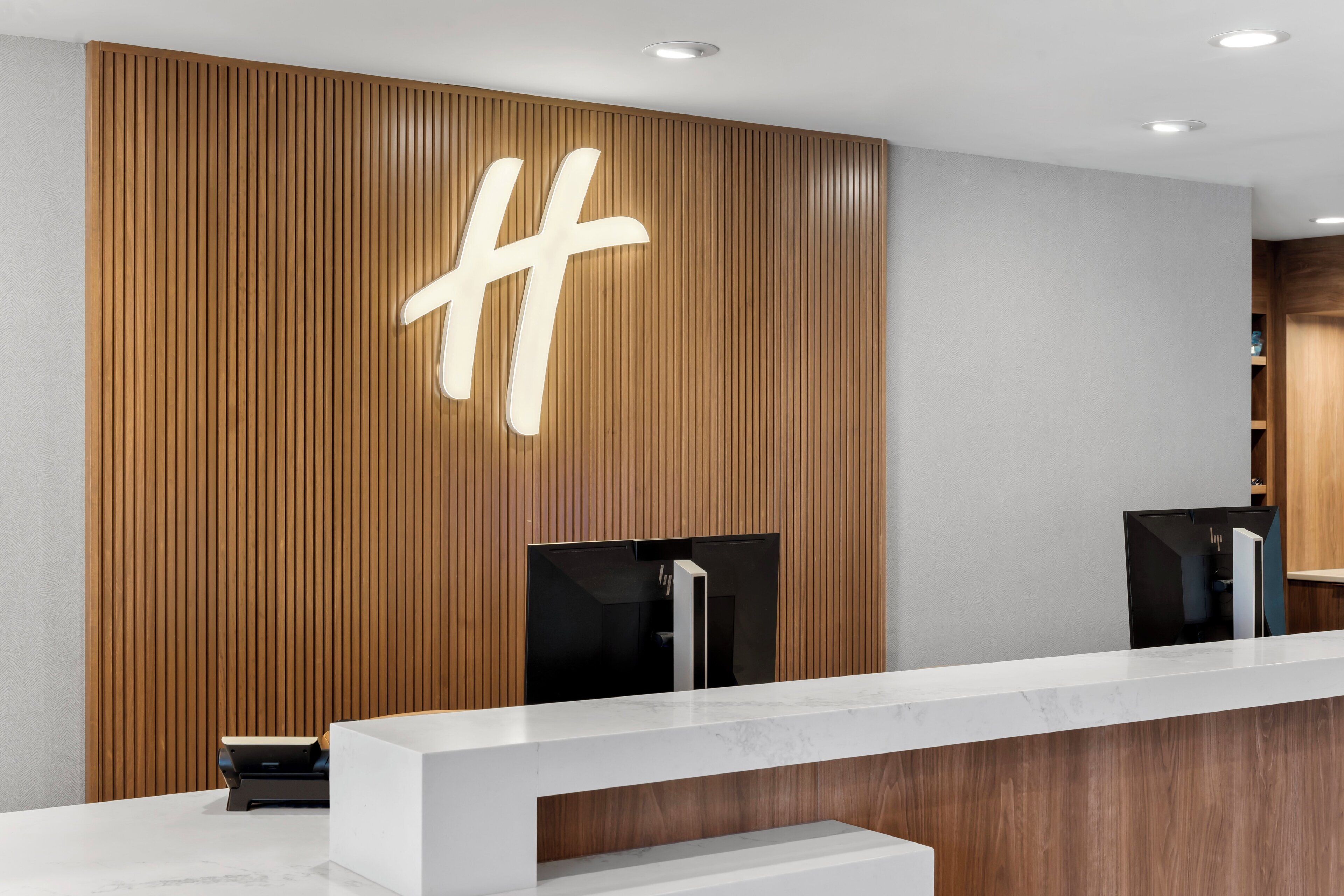 Eine Rezeption mit einer Wandpaneele aus Holz und einem großen, beleuchteten ‚H‘-Schild.