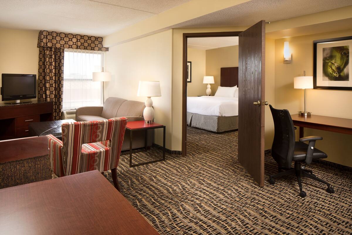 A hotel room with a bed, a desk, a chair, a TV, and a patterned carpet.