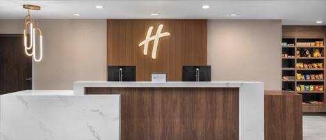 A reception desk with a wooden panel and a marble counter, two black speakers, and a sign with a large 'H' logo.