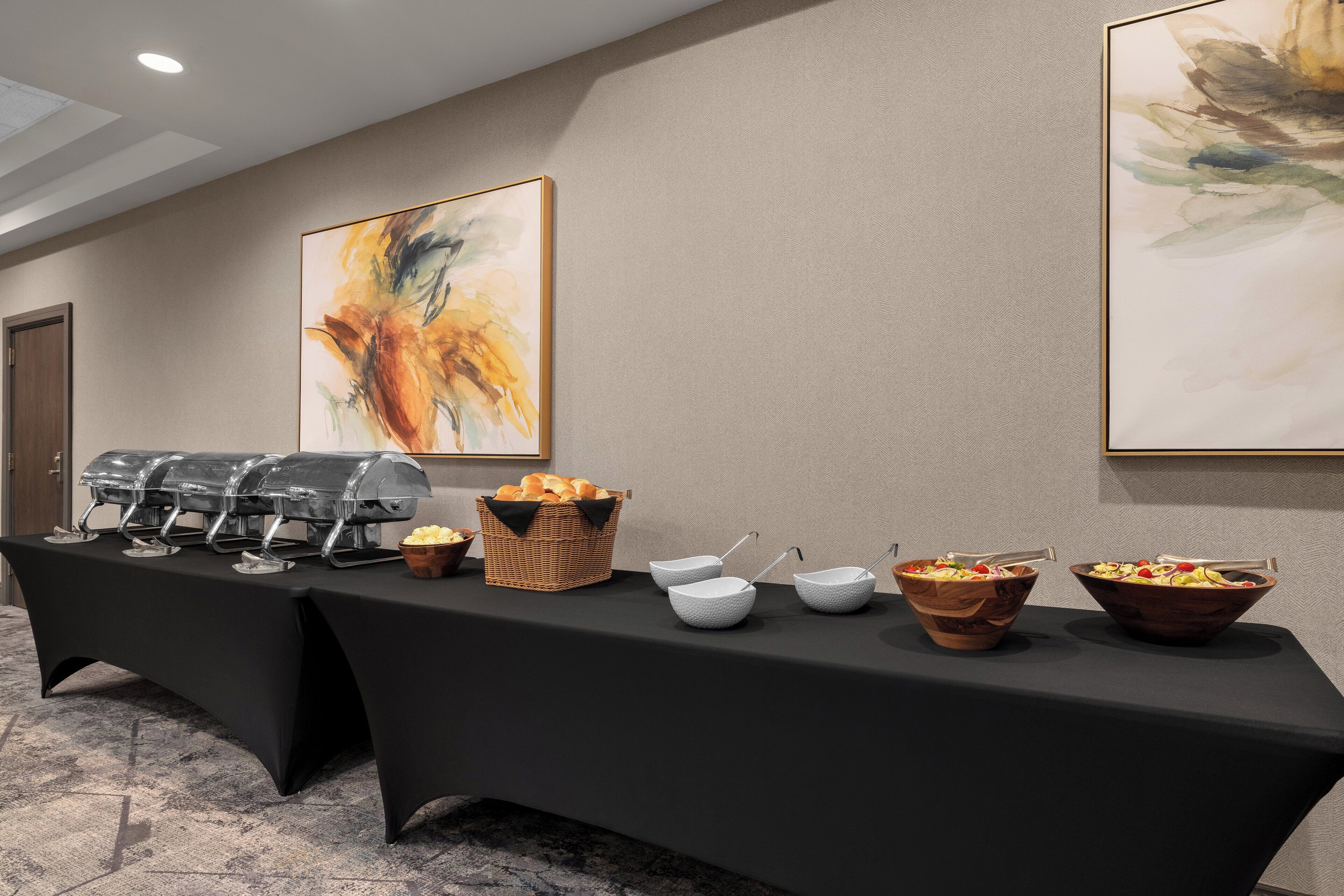 A buffet table with various food items and a large abstract painting on the wall.