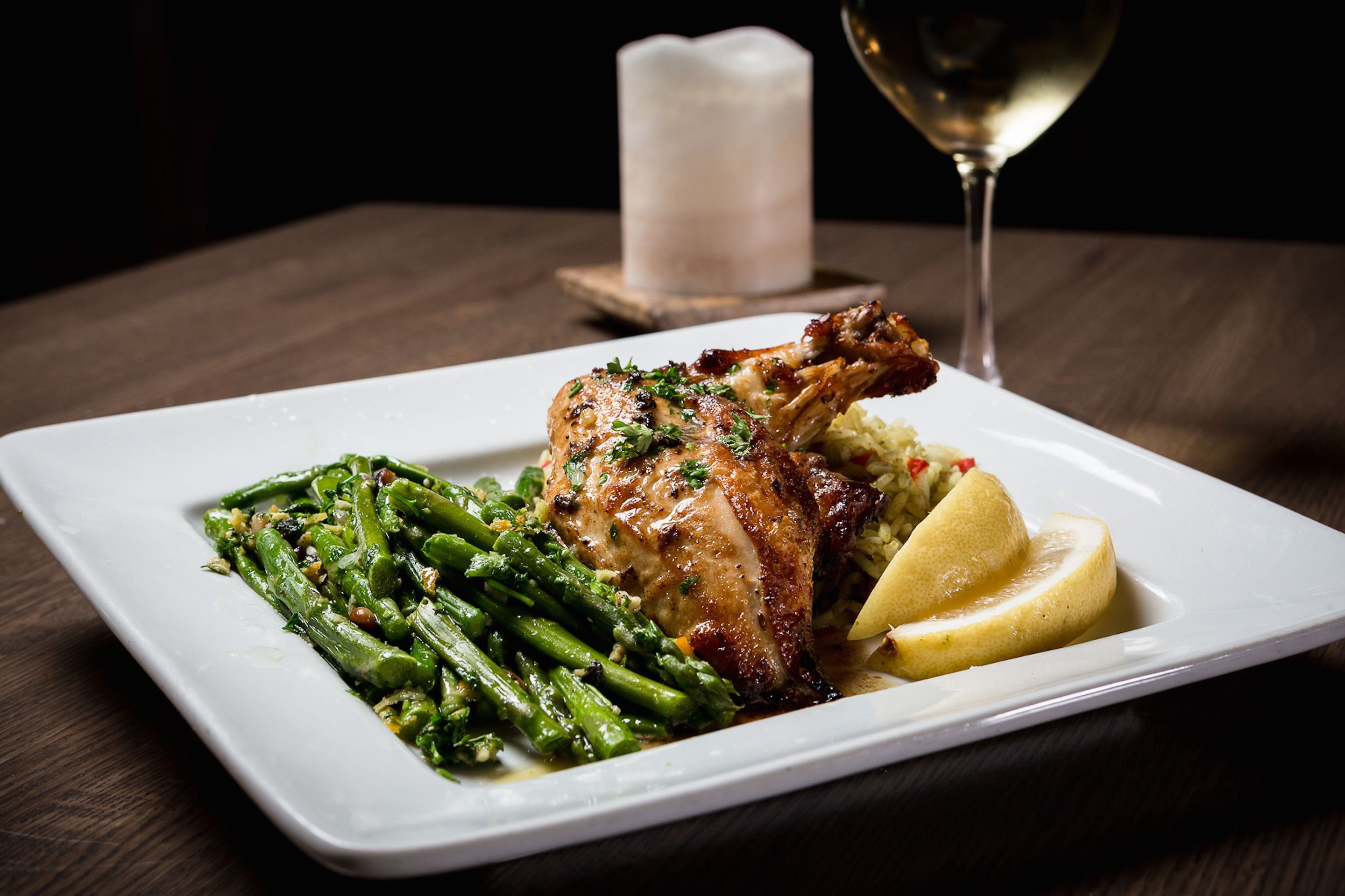 Un plato blanco cuadrado con pollo asado, judías verdes y rodajas de limón.