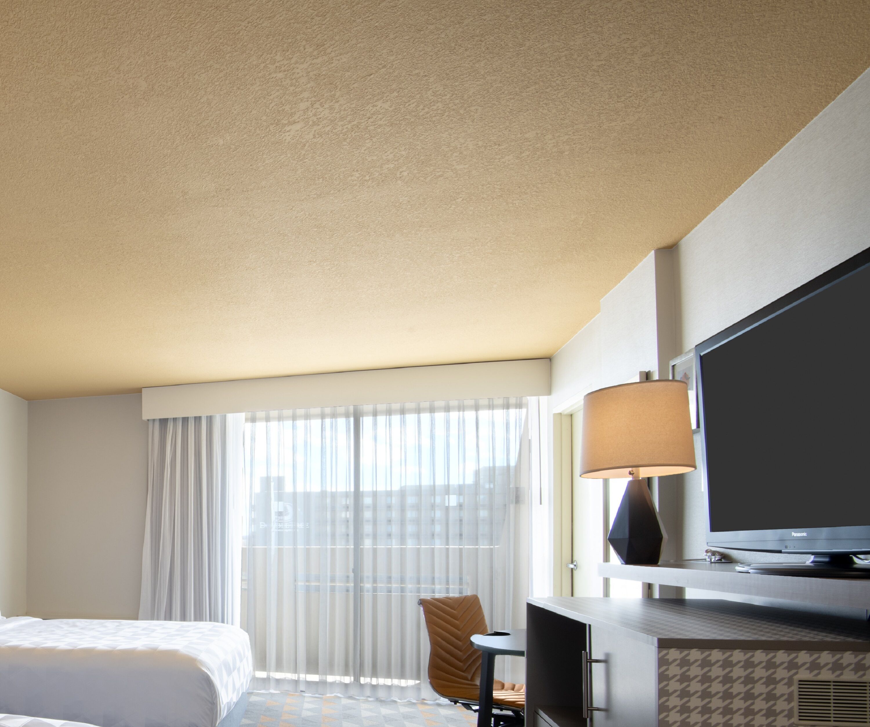 A hotel room with a bed, a desk, a chair, a television, and a window with curtains.