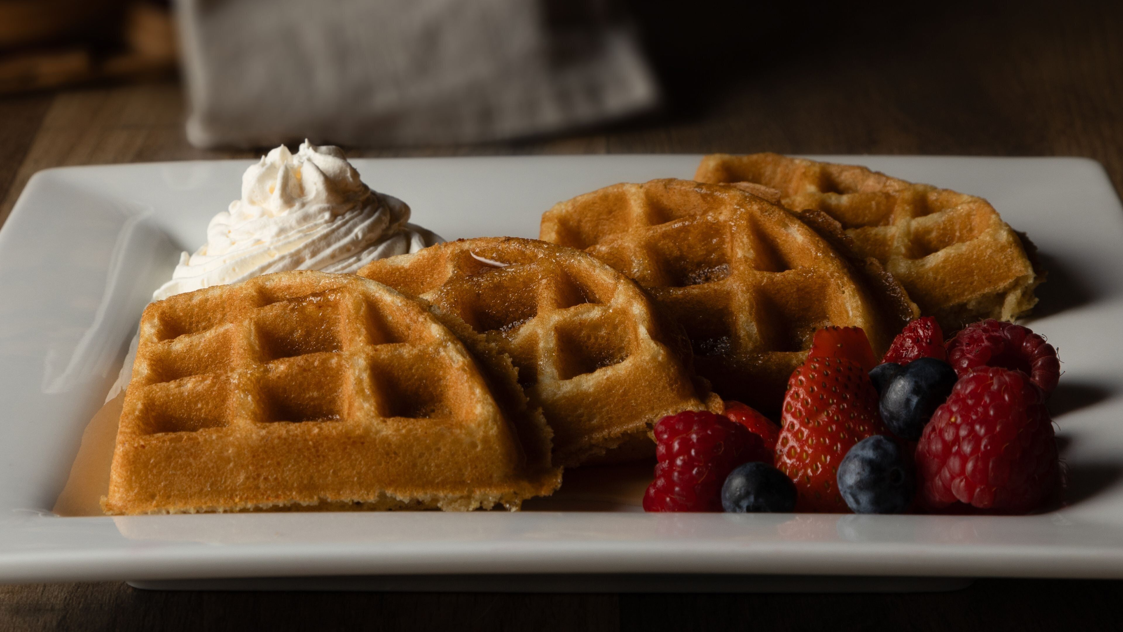 A plate with waffles and whipped cream, accompanied by fresh berries.