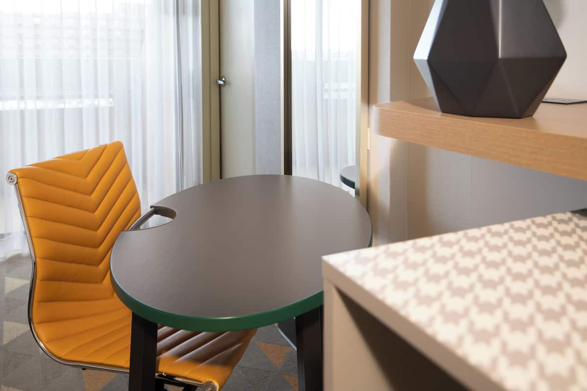 A modern room with a round table, a yellow chair, and a geometric lamp on a wooden shelf.