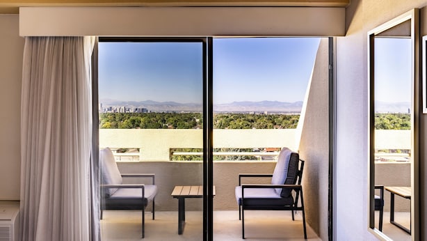 Ein Hotelzimmer mit einer Schiebetür zu einem Balkon, der zwei Stühle und einen kleinen Tisch bietet.