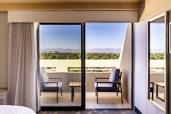 A hotel room with a sliding glass door leading to a balcony with two chairs and a small table.