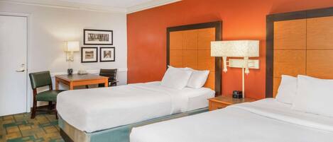A hotel room with two beds, a desk, a chair, and a lamp.