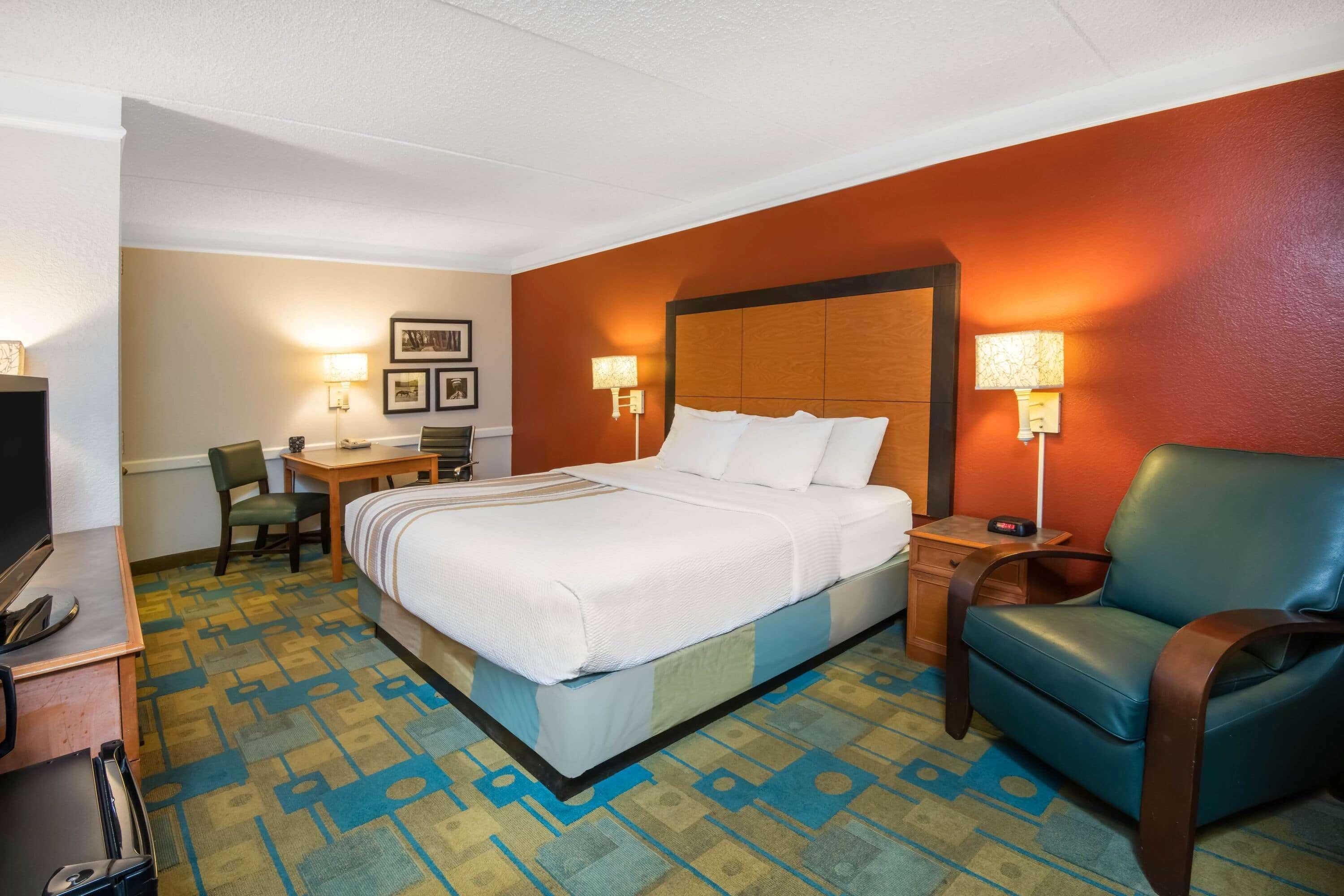 A hotel room with a bed, a desk, a chair, and a TV.