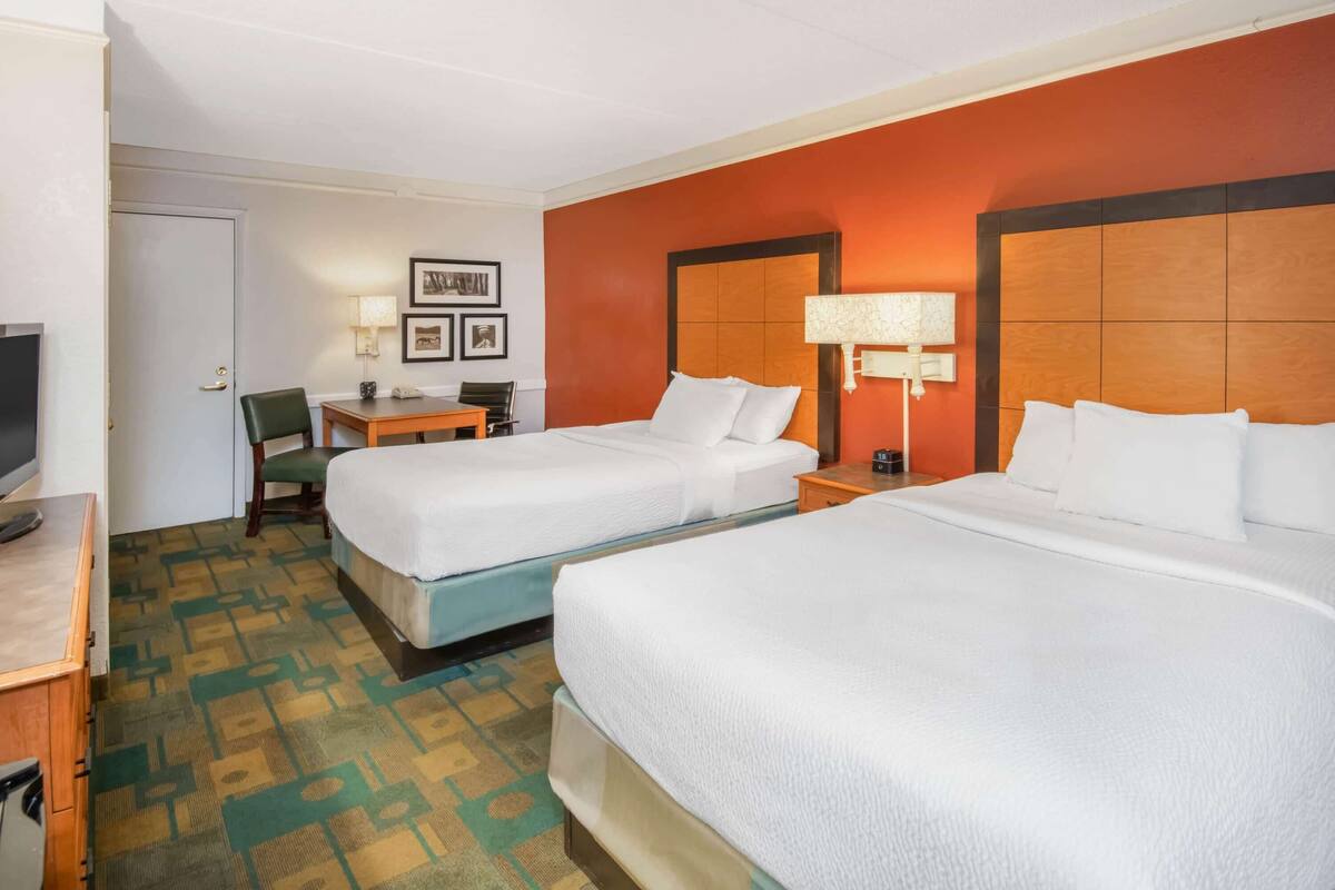 A hotel room with two beds, a desk with a chair, a TV, and framed pictures on the wall.