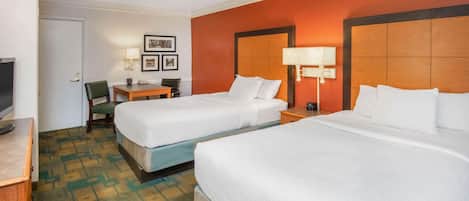 A hotel room with two beds, a desk with a chair, a TV, and framed pictures on the wall.