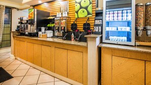 A self-service counter with a coffee machine, waffle maker, and refrigerated display of beverages and snacks.