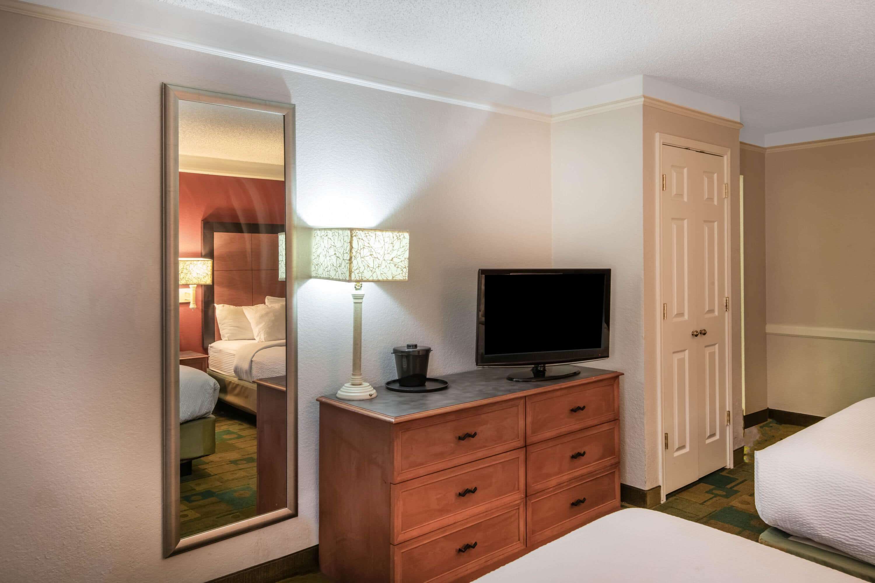 A hotel room with a bed, a TV on a wooden dresser, a mirror, and a door.