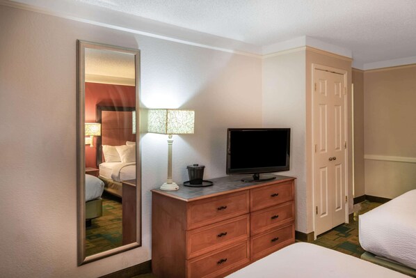 Una habitación de hotel con una cama, un televisor en una cómoda de madera, un espejo y una puerta.