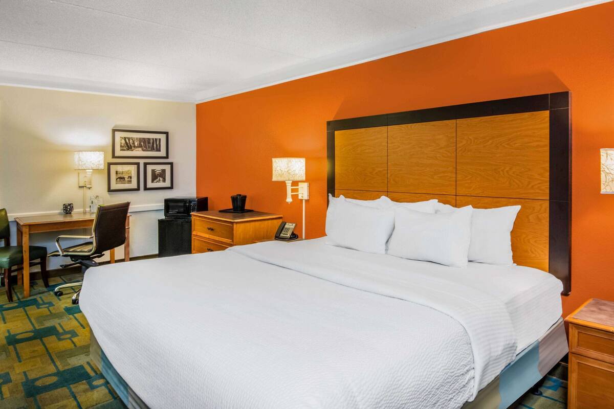 A hotel room with a large bed, a desk with a chair, a telephone, and framed pictures on the wall.