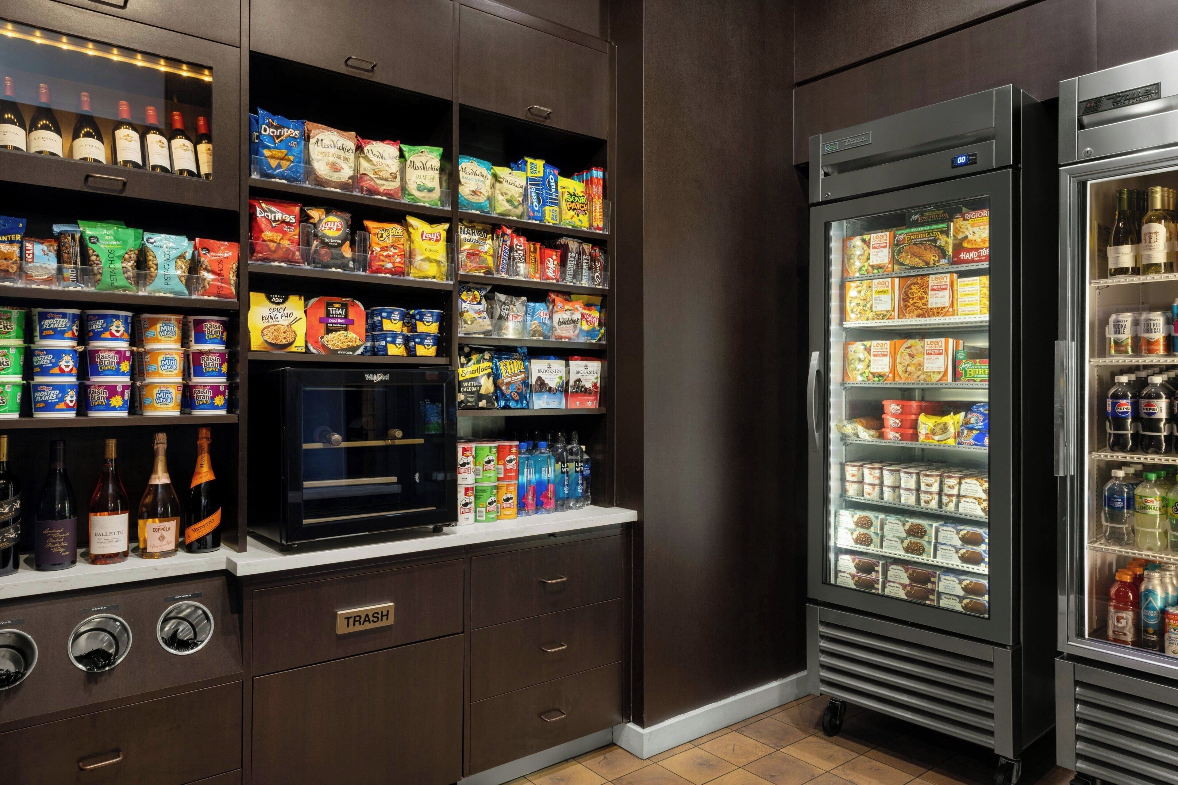 A kitchenette with a wine cooler, a coffee machine, and shelves stocked with snacks and condiments.