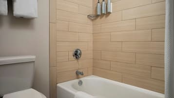 Un baño moderno con inodoro, bañera y un estante con artículos de aseo.