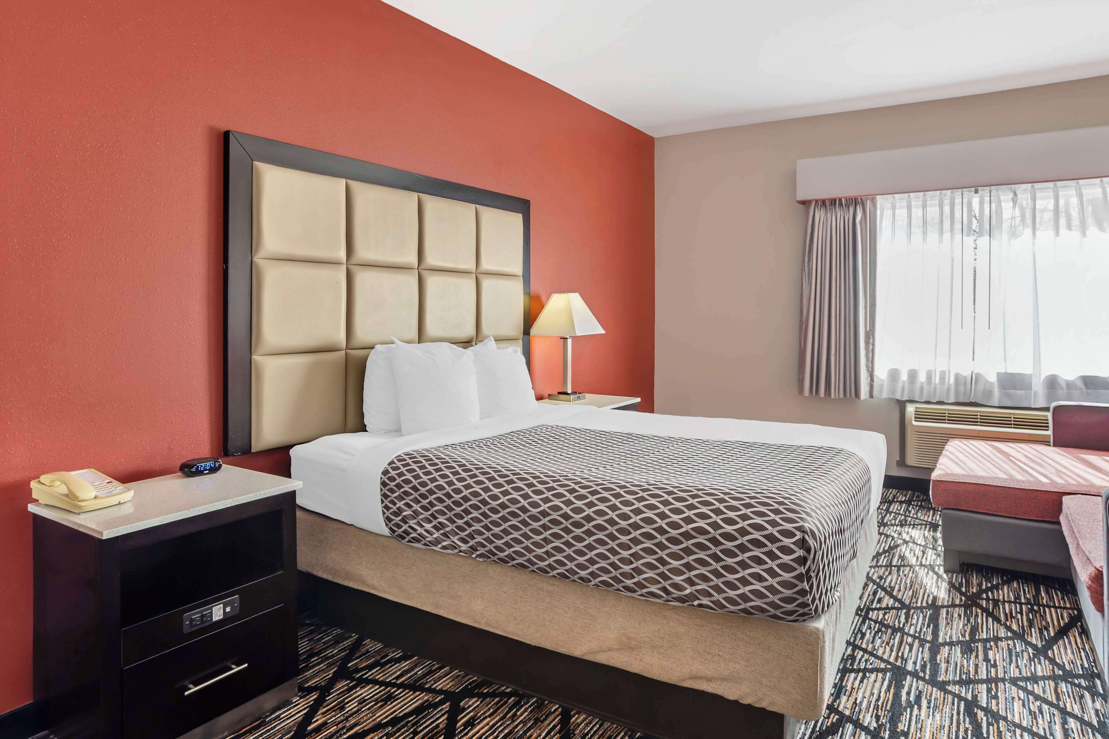 A hotel room with a large bed, a bedside table with a lamp, a telephone, and a small desk with drawers.