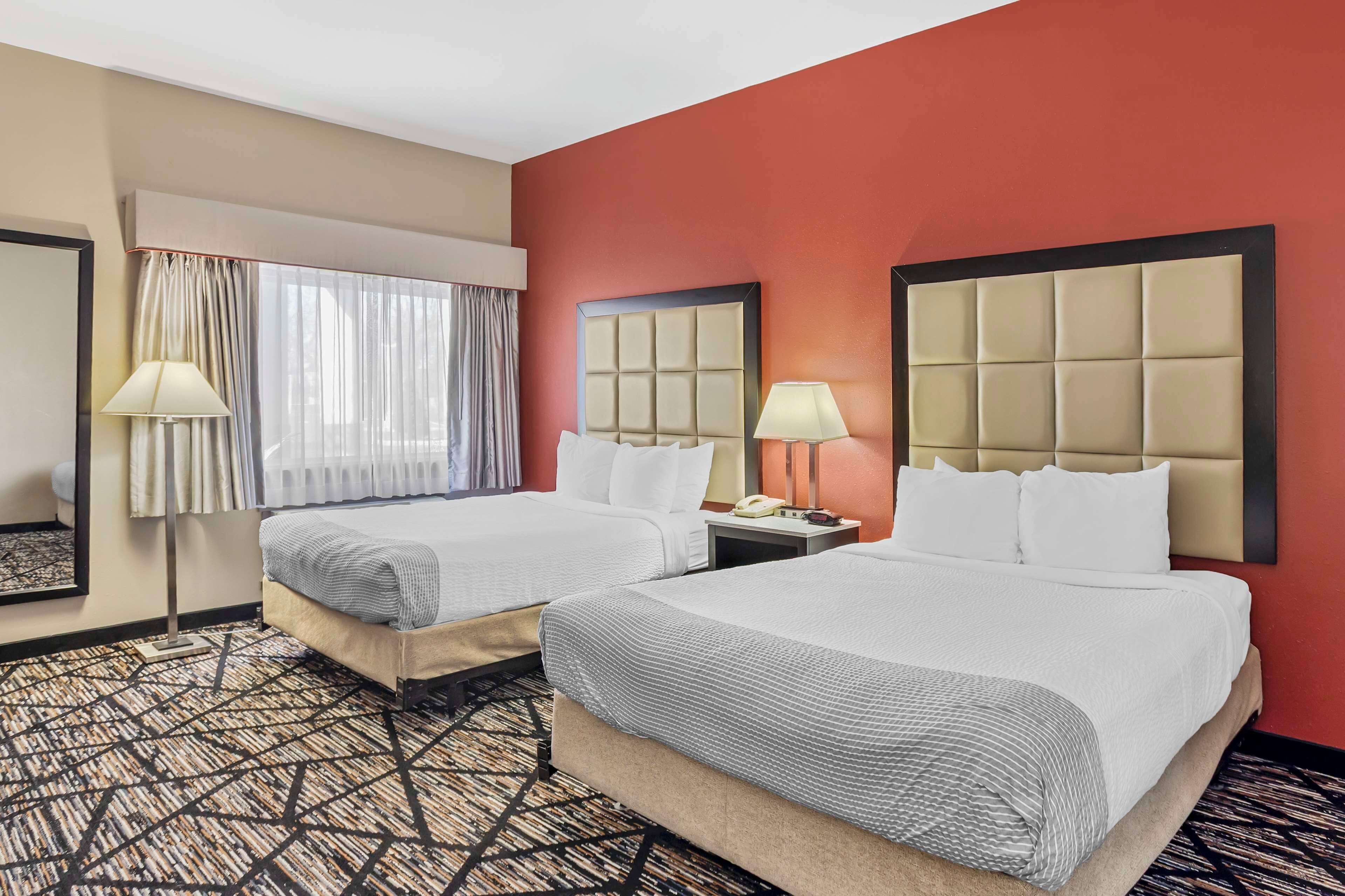 Una habitación de hotel con dos camas, un espejo grande, una ventana con cortinas y una alfombra estampada.