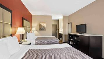 A hotel room with two beds, a TV, a desk with a lamp, and a wardrobe.
