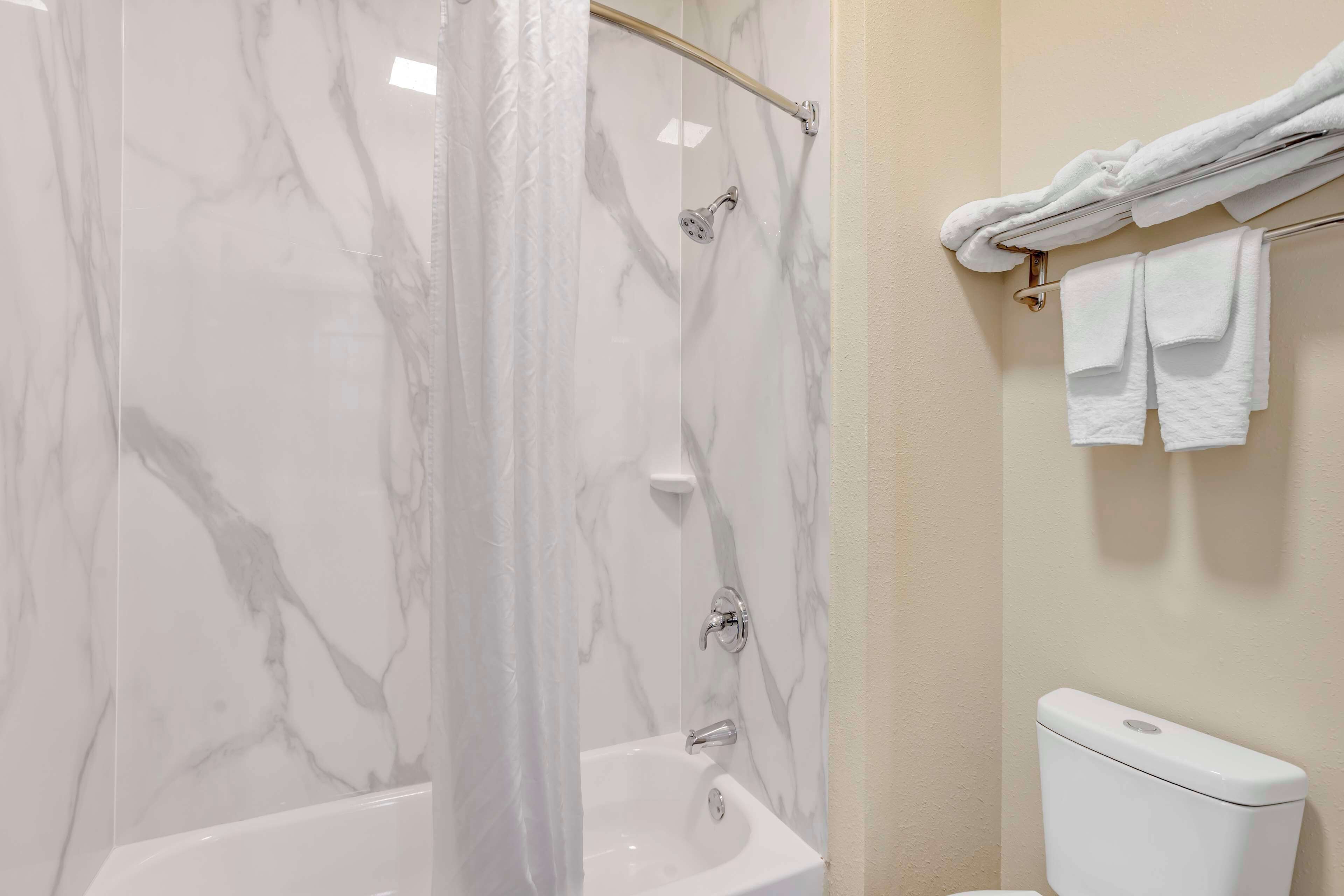 A bathroom with a marble shower enclosure, a white bathtub, and a toilet.