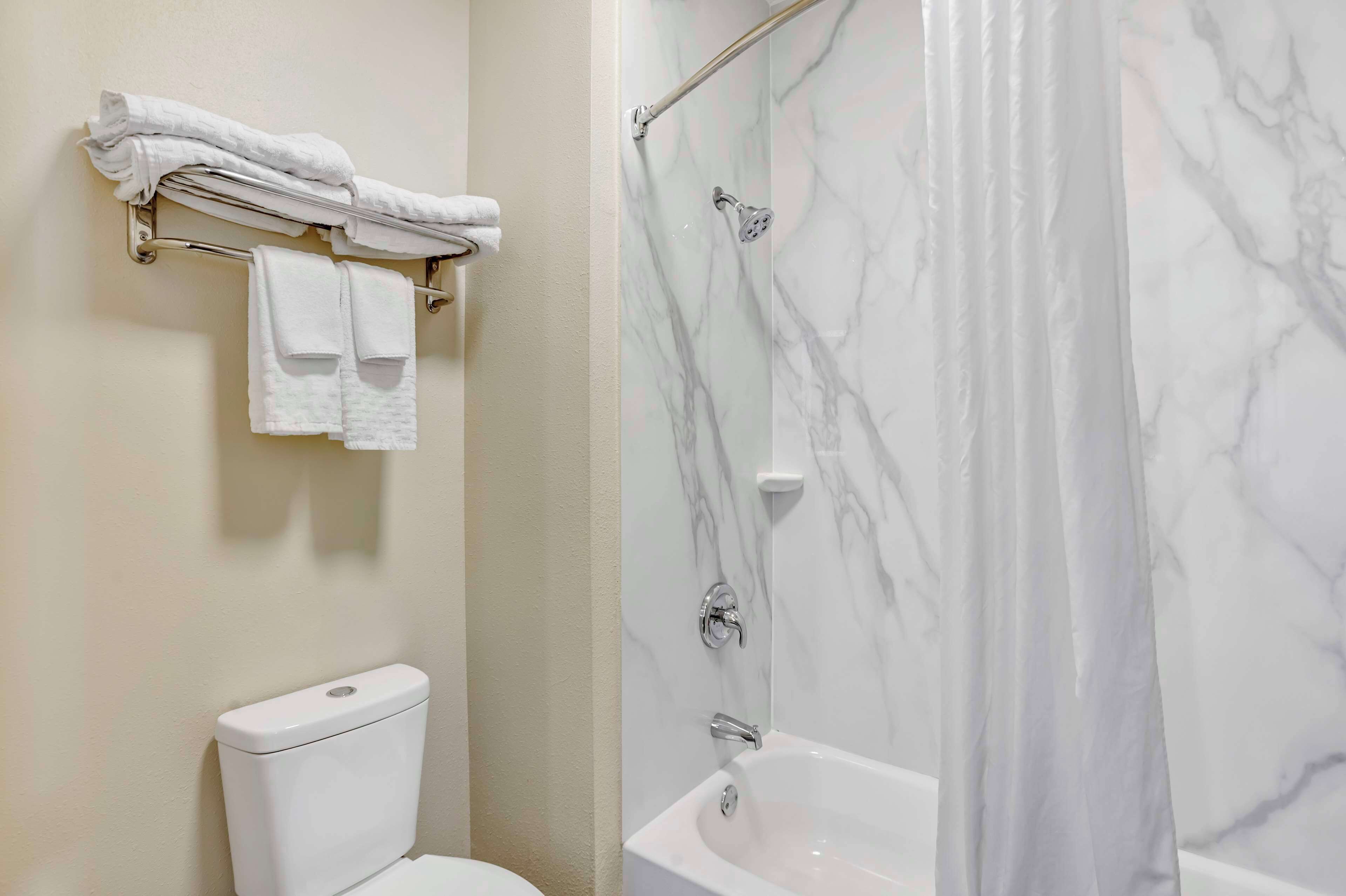 A bathroom with a toilet, a shower with a marble wall, and a towel rack with folded towels.