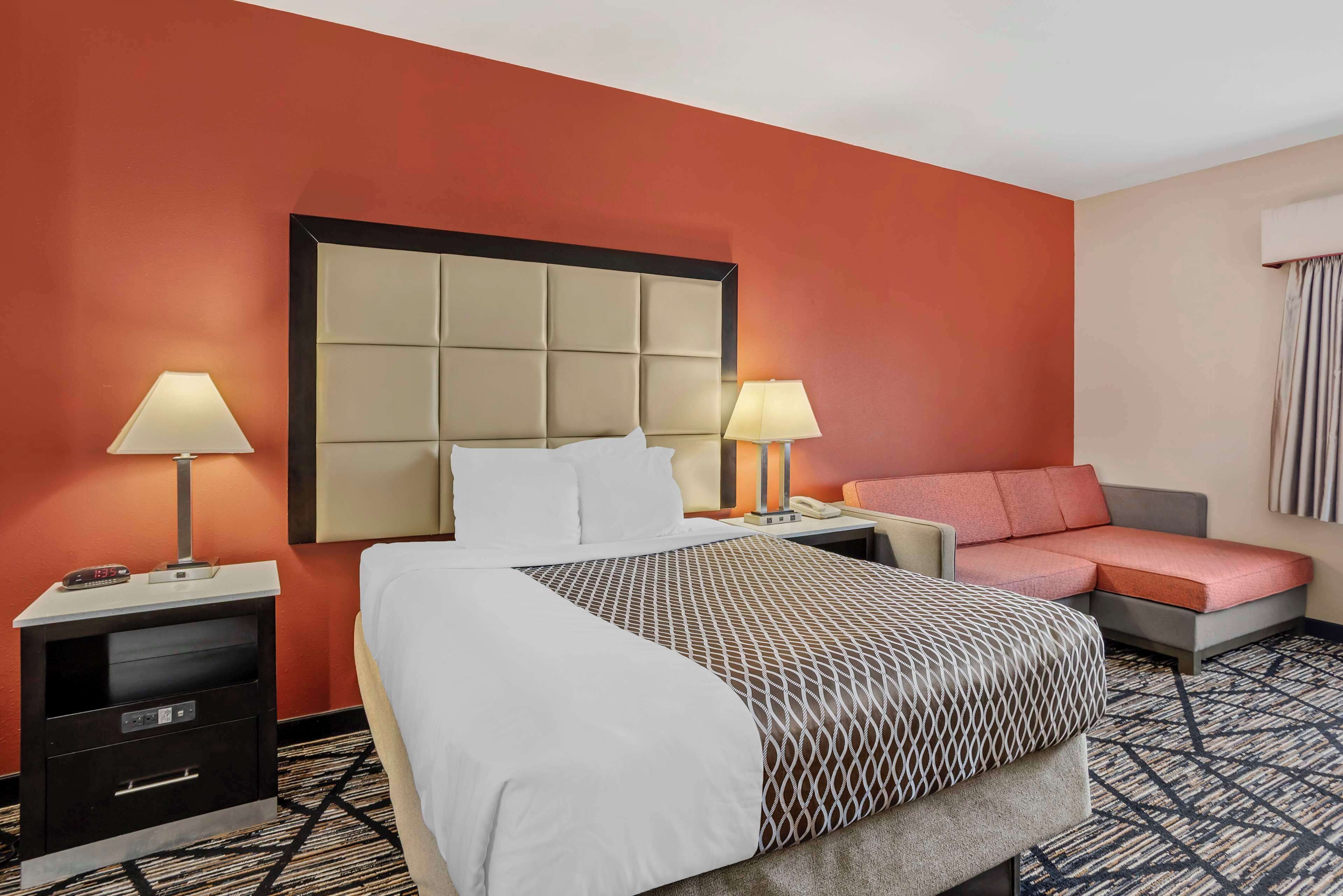A hotel room with a large bed, two bedside tables with lamps, a sofa, and a patterned carpet.