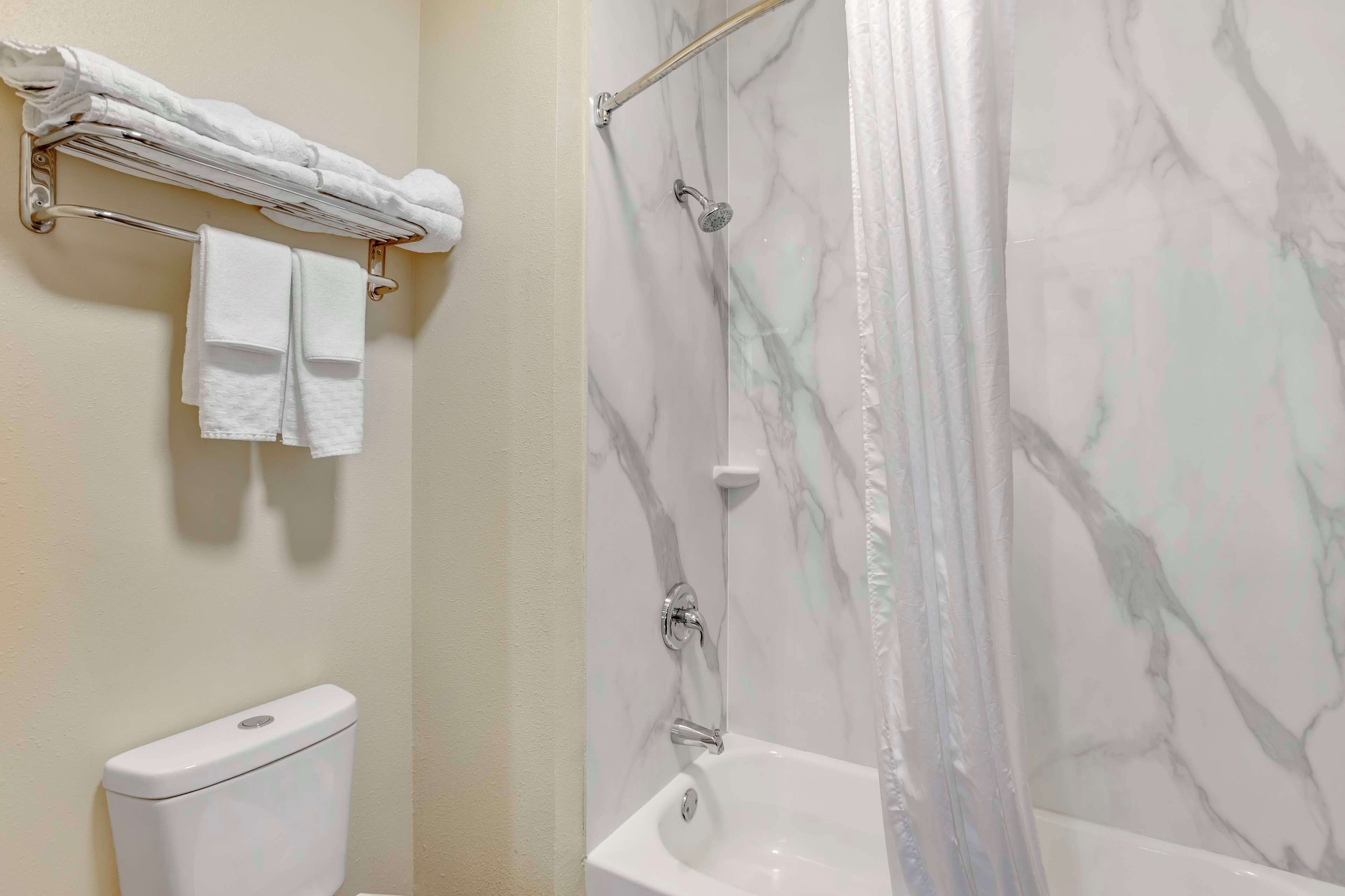 A bathroom with a toilet, a shower with a glass door, and a towel rack with folded towels.