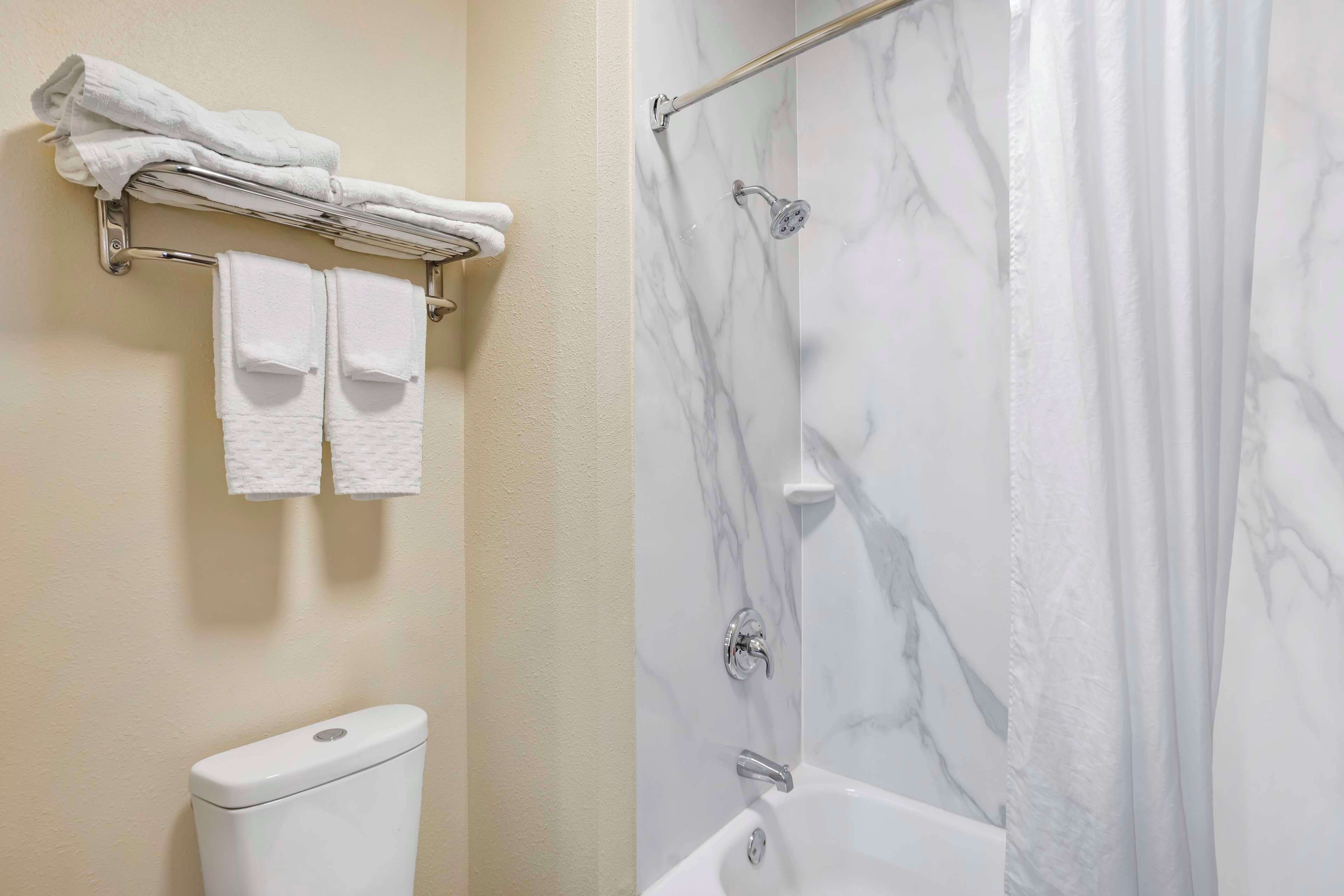Une salle de bain comprenant des toilettes, un porte-serviettes avec des serviettes pliées, une douche avec une porte en verre et une baignoire.