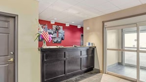 A reception area with a dark wooden counter, a red wall with a car and American flag decoration, and a glass door with a caution sign. - Best Western Carlisle (Carlisle)