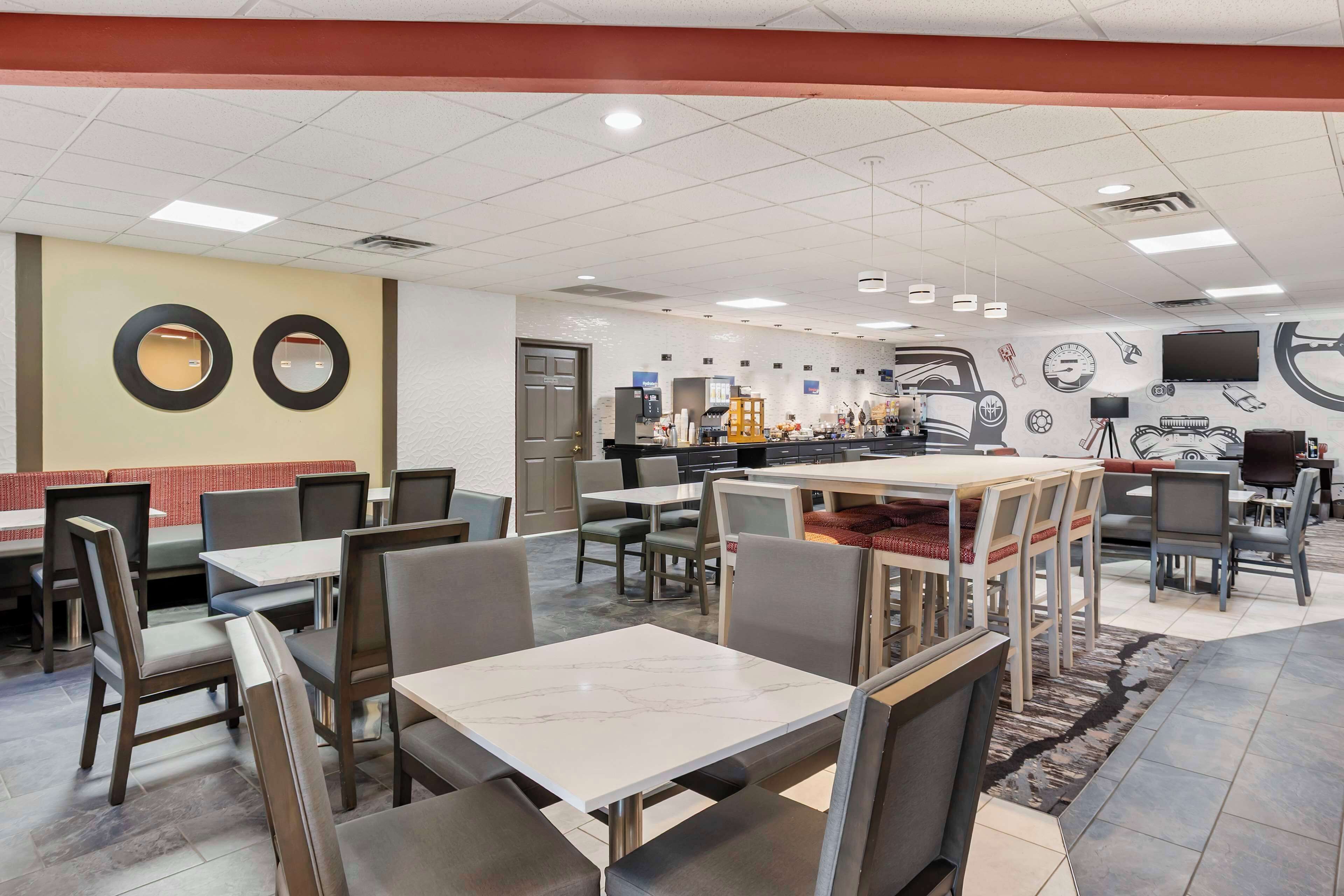 A restaurant with multiple tables and chairs, a counter, and a wall with various items like a clock and a TV.