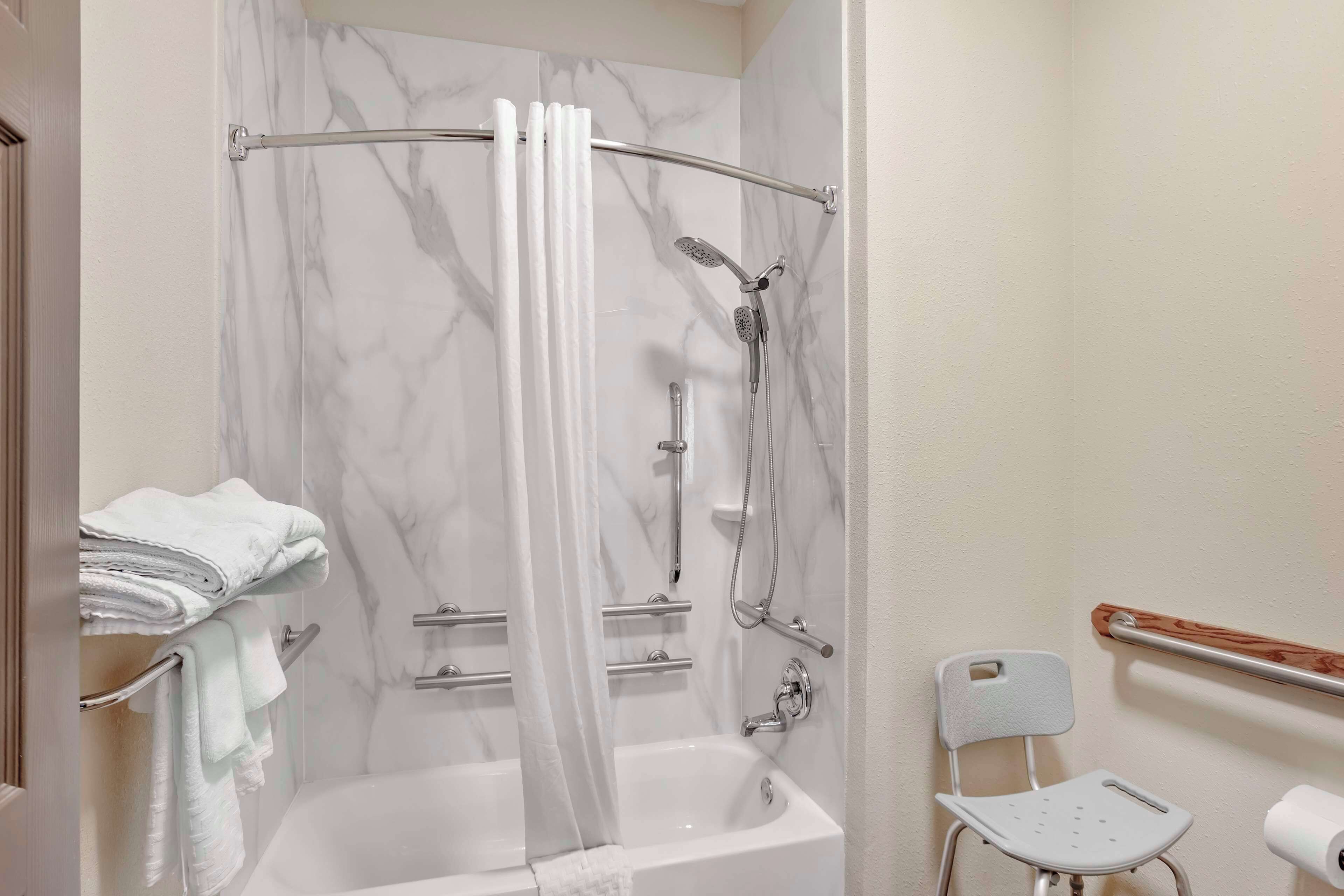A bathroom with a bathtub, a shower with a glass door, a toilet, and a chair.