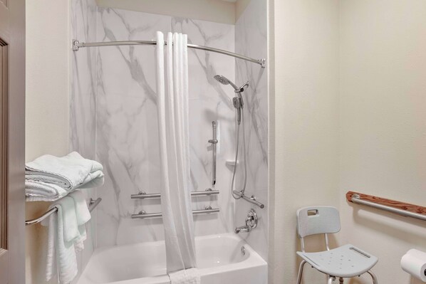 Un baño con bañera, ducha con puerta de vidrio, inodoro y una silla.