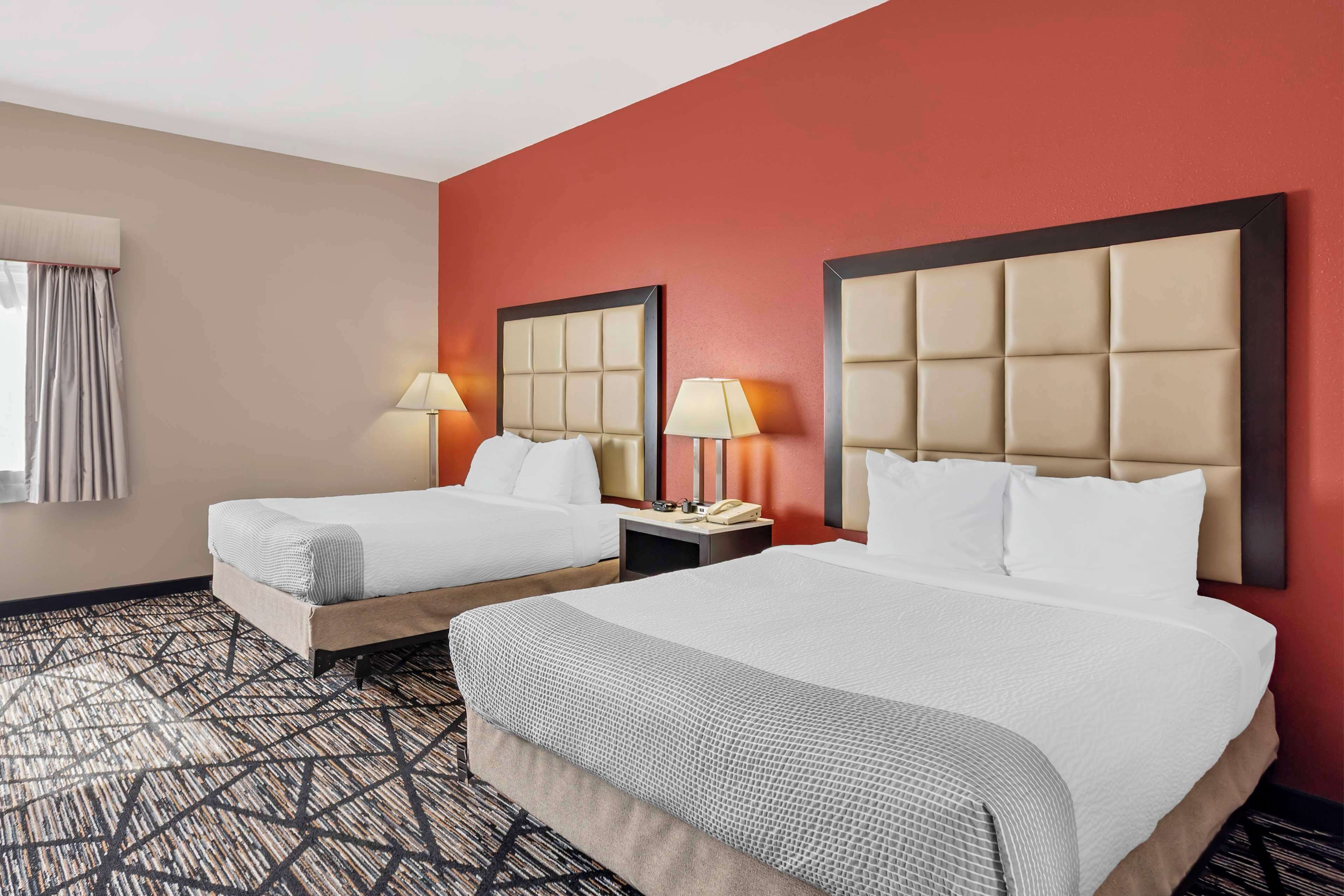 Une chambre d’hôtel avec deux lits, un mur d’accent rouge et une moquette à motifs.