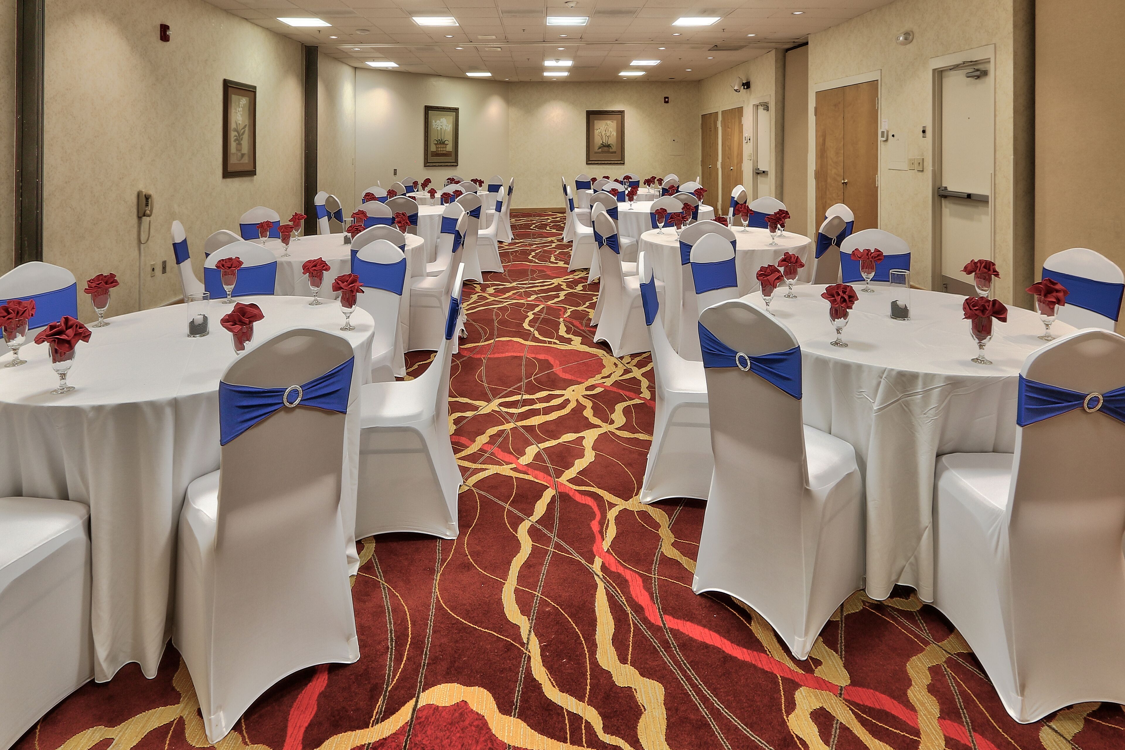 A conference room with round tables, white chairs with blue sashes, and red flower arrangements on each table.