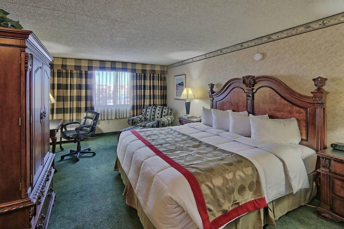 A hotel room with a large bed, a desk with a lamp, a chair, and a wardrobe.