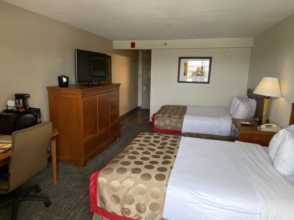 A hotel room with two beds, a desk with a computer, a television on a wooden cabinet, and a lamp on the nightstand.