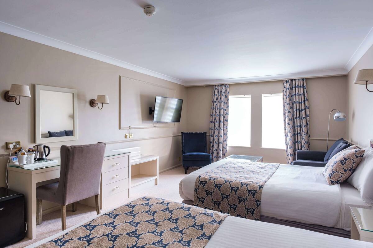 A hotel room with two beds, a desk, a chair, a TV, and a window with curtains.