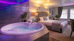 A modern hotel room with a large oval bathtub, a comfortable bed, a bedside table, and a view of the outdoors. - Moor Hall Hotel, BW Premier Collection (Sutton Coldfield)