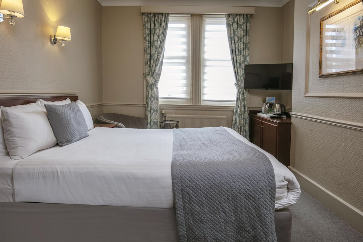 A hotel room with a bed, a television, a radiator, and a window with curtains.