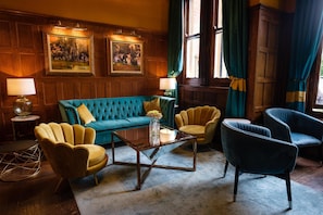 A room with a teal sofa, yellow armchairs, a glass coffee table, wooden paneled walls, and framed artwork. - Moor Hall Hotel, BW Premier Collection (Sutton Coldfield)