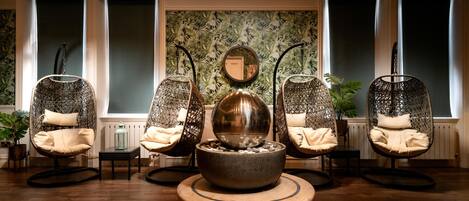 A room with four wicker chairs, a central table with a spherical object, and a wall with a tropical leaf pattern.
