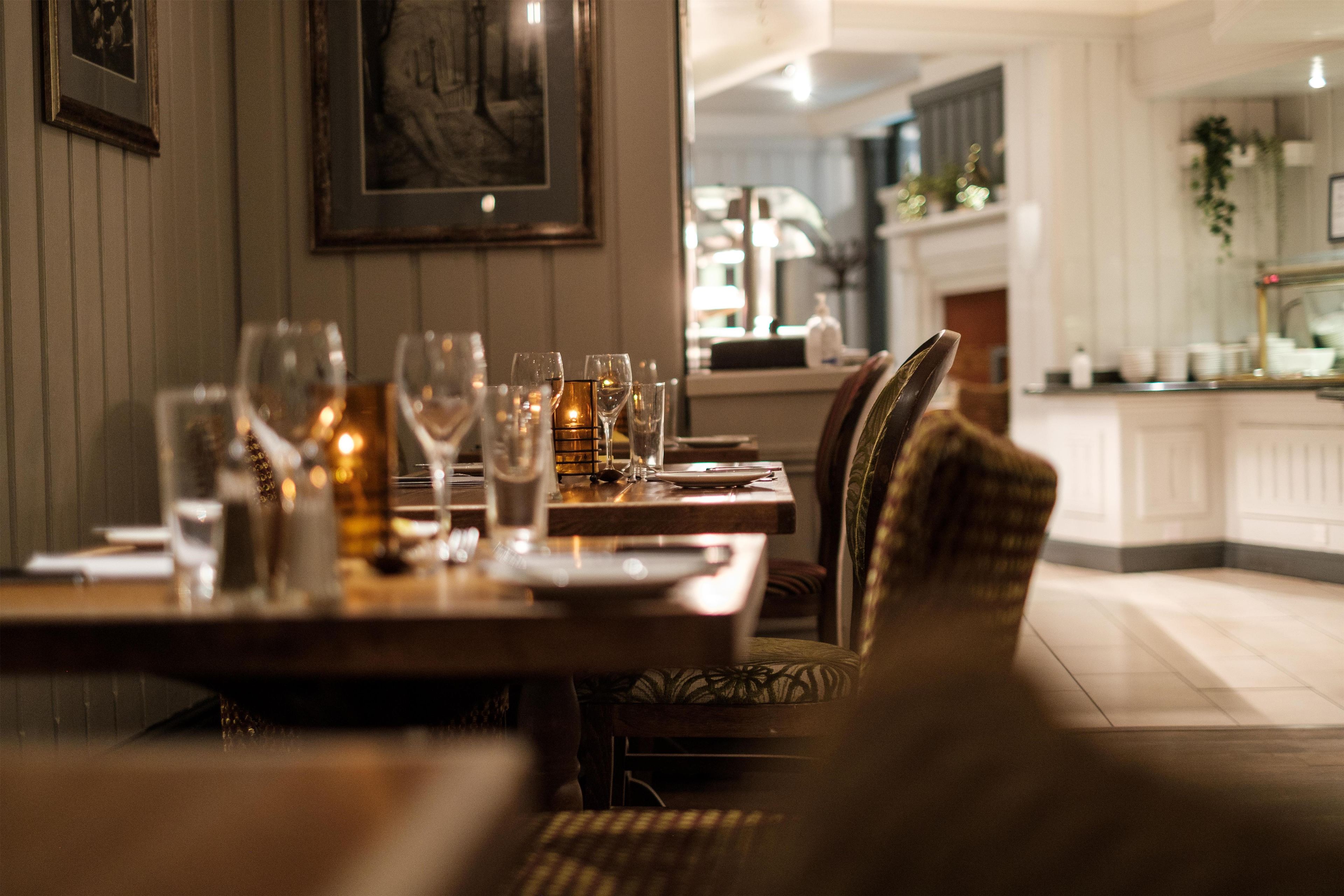 A dining area with tables set for a meal, chairs, and a view of the kitchen in the background.