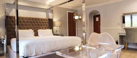 A modern hotel room with a large bed, a glass dining table, and a separate seating area.