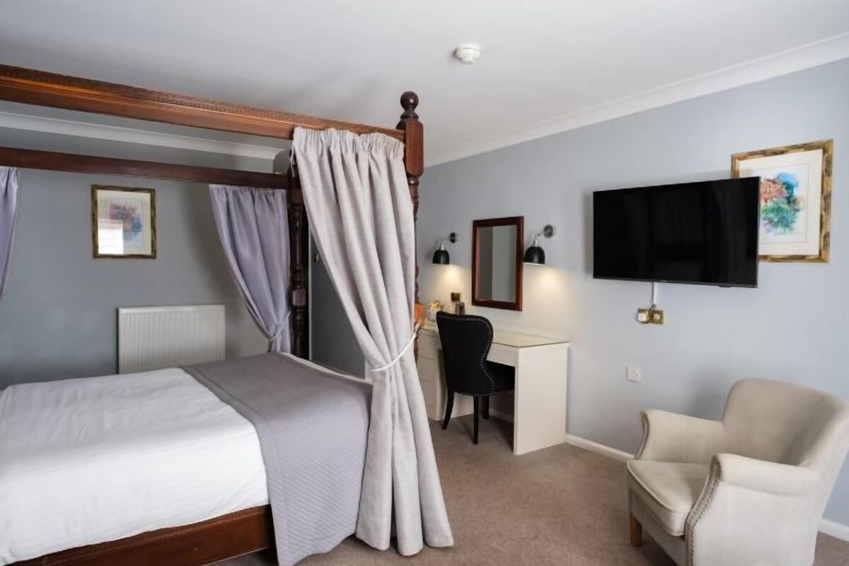 Une chambre d’hôtel avec un lit à baldaquin, un bureau, une chaise et une télévision.