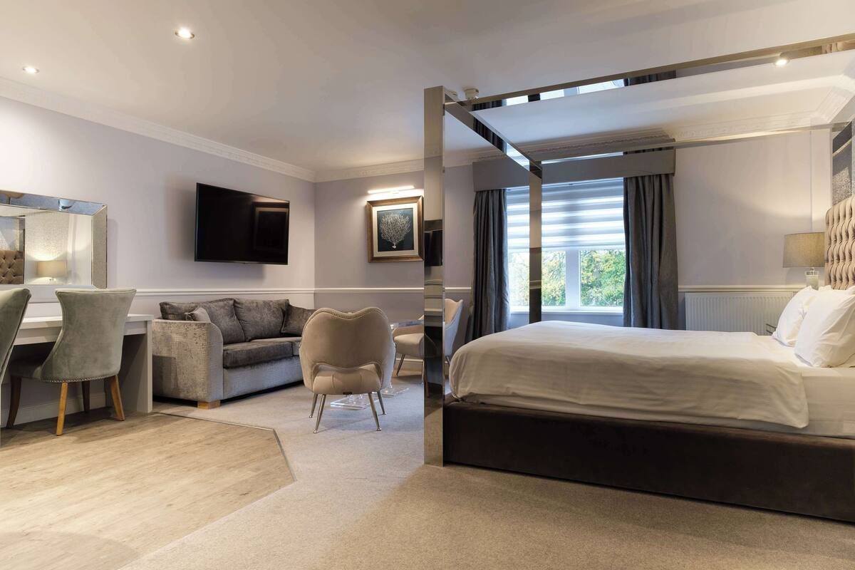 A modern hotel room with a large bed, a desk with a chair, a sofa, and a TV mounted on the wall.