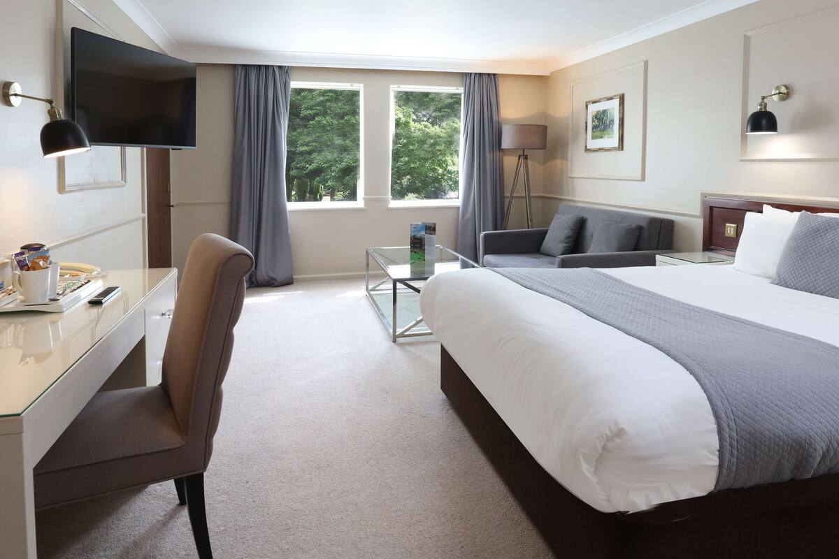 A hotel room with a bed, a desk, a chair, a TV, and a window with curtains.