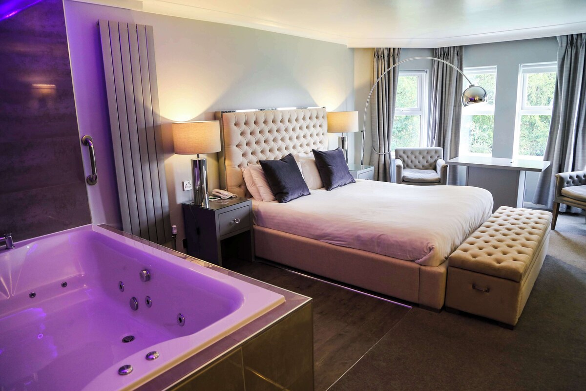 Een moderne hotelkamer met een groot bed, een aparte zithoek, een badkuip en een bureau.
